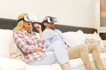 Couple sitting on couch at home using Virtual Reality Glasses - MAEF011431