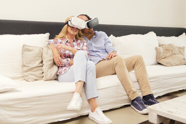 Paar sitzt Kopf an Kopf auf der Couch zu Hause und benutzt eine Virtual-Reality-Brille - MAEF011432