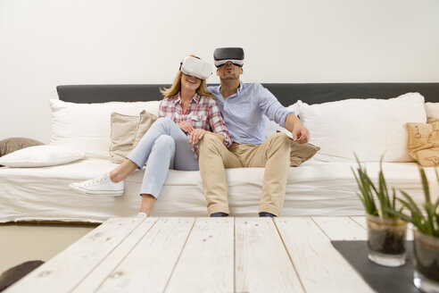 Paar sitzt nebeneinander auf der Couch zu Hause und benutzt eine Virtual-Reality-Brille - MAEF011433