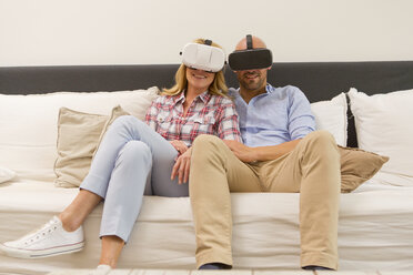 Smiling couple sitting side by side on couch at home using Virtual Reality Glasses - MAEF011434