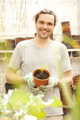 Lächelnder Mann hält Blumentopf mit Moringa-Setzling - MFRF000514