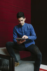 Young businessman sitting on armchair of a lobby using his digital tablet - BOYF000230