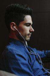 Profil eines jungen Mannes, der mit Kopfhörern Musik hört, vor einem schwarzen Hintergrund - BOYF000237