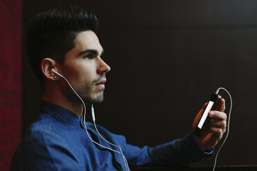 Profile of young man hearing music with earphones in front of black background - BOYF000238