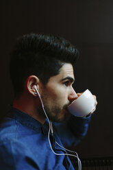 Profile of young man hearing music with earphones while drinking coffee in front of black background - BOYF000239