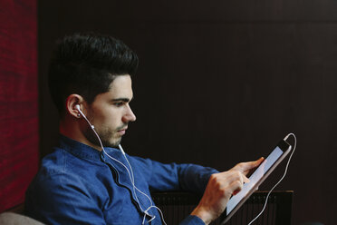 Profile of young businessman with earphones using digital tablet in front of black background - BOYF000241