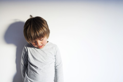 Kleiner Junge steht vor einer Mauer und schaut nach unten, lizenzfreies Stockfoto