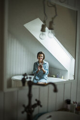 Junge Frau im Badezimmer mit Smartphone - HAPF000286