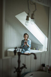 Young woman in bathroom using smartphone - HAPF000286