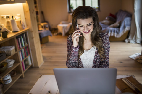 Junge Frau zu Hause bei der Arbeit mit Laptop, lizenzfreies Stockfoto