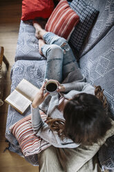 Junge Frau zu Hause mit einer Tasse Kaffee und einem Buch - HAPF000302