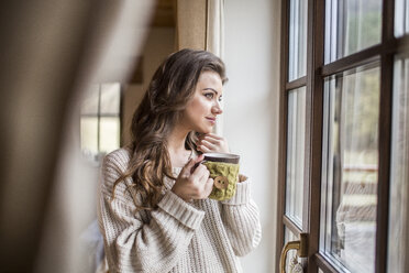 Junge Frau zu Hause, die mit einer Tasse Kaffee aus dem Fenster schaut - HAPF000317