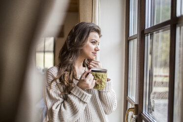 Young woman at home looking out of window with cup of coffee - HAPF000317