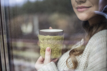 Young woman standing at window with cup of coffee - HAPF000318