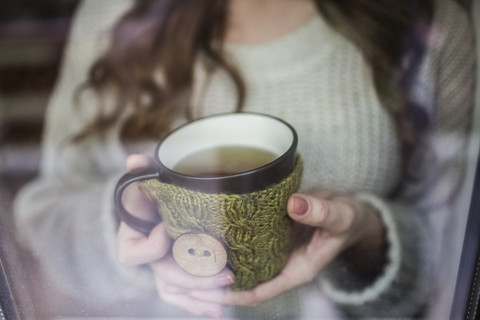 Junge Frau am Fenster stehend mit einer Tasse Tee, lizenzfreies Stockfoto