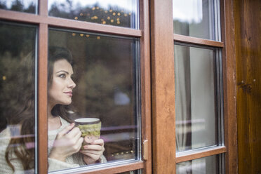 Junge Frau am Fenster stehend mit einer Tasse Kaffee - HAPF000320