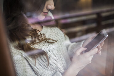 Junge Frau steht am Fenster und benutzt ihr Smartphone - HAPF000322