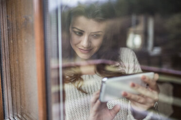 Junge Frau steht am Fenster und benutzt ihr Smartphone - HAPF000323