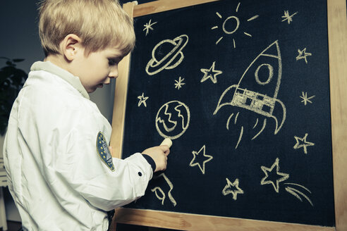 Kind mit Astronautenanzug, das Himmelskörper und Leuchtkörper auf eine Kreidetafel zeichnet - MFF002951