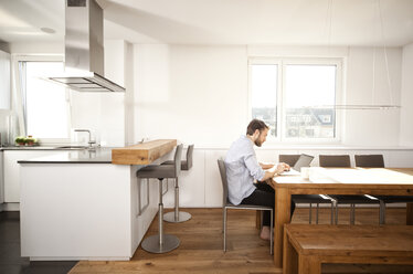 Man sitting at table in his open plan kitchen using laptop - MFRF000527