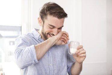 Lachender junger Mann mit einem Glas Milch, der sich den Mund abwischt - MFRF000541