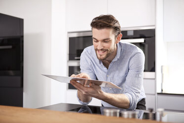 Portrait of smiling young man using digital tablet in his kitchen - MFRF000550