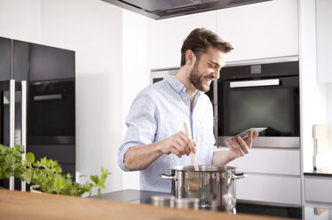 Young man looking at with mini tablet while cooking - MFRF000552