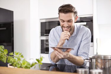 Portrait of smiling young man with mini tablet in his kitchen - MFRF000553