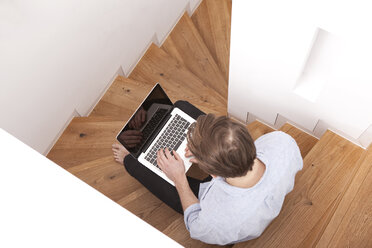 Mann sitzt auf Holzstufen und benutzt einen Laptop - MFRF000562