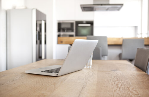 Laptop auf einem Holztisch in einer offenen Küche - MFRF000590