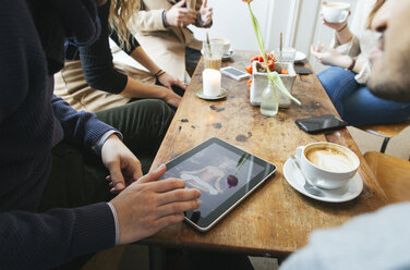 Man in a cafe showing picture on digital tablet to friends - JUBF000124