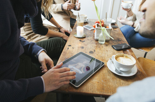 Mann in einem Café zeigt Freunden ein Bild auf einem digitalen Tablet - JUBF000124