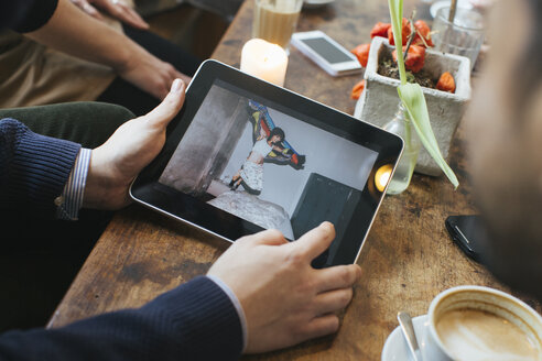 Man in a cafe showing picture on digital tablet to friends - JUBF000125