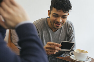 Zwei Männer in einem Café betrachten einen Fotoabzug - JUBF000130