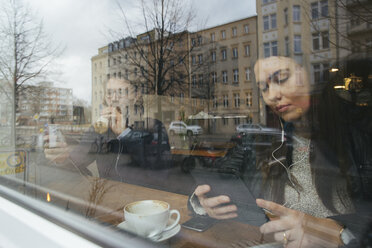 Frau in einem Café hinter einer Fensterscheibe mit digitalem Tablet - JUBF000134