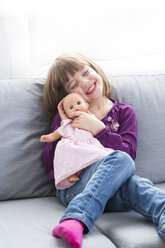 Portrait of happy little girl sitting with her doll on the couch - LVF004698