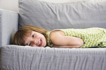 Porträt eines lächelnden kleinen Mädchens, das auf der Couch liegt - LVF004704