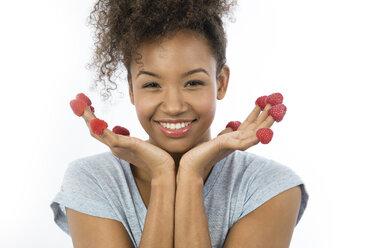 Portrait of smiling young woman with raspberries on her fingertips in front of white background - GDF000977
