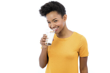 Portrait of smiling young woman drinking glass of milk in front of white background - GDF000981