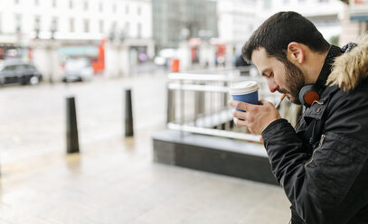 UK, London, Mann mit Kaffee zum Mitnehmen, der sich eine Zigarette anzündet - MGOF001691