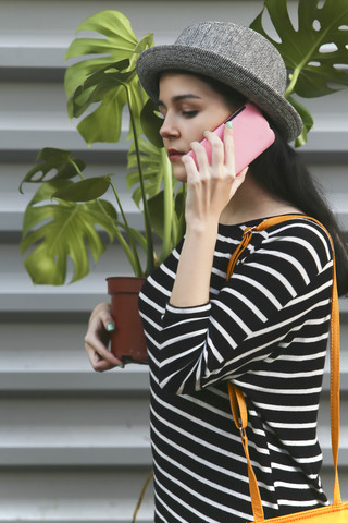 Frau telefoniert mit Smartphone und trägt eine Monstera deliciosa, lizenzfreies Stockfoto