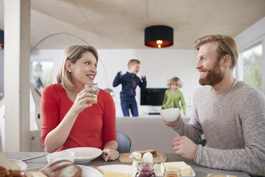 Eltern beim Frühstück zu Hause mit Kindern im Hintergrund - RHF001394