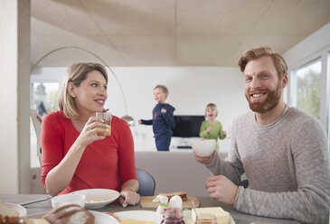 Parents having breakfast at home with children in background - RHF001395