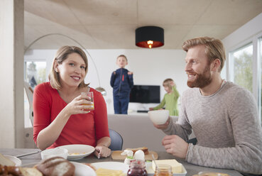 Eltern beim Frühstück zu Hause mit Kindern im Hintergrund - RHF001397