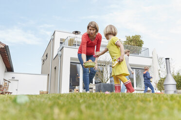 Pregnant mother with children in garden looking for Easter eggs - RHF001424