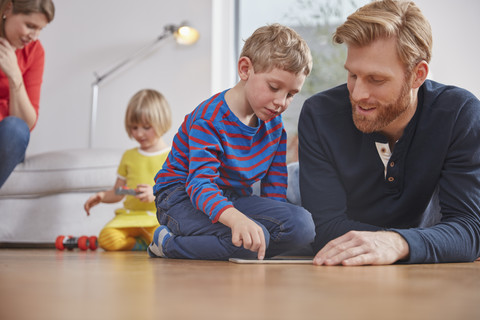 Fathar und sein Sohn benutzen ein digitales Tablet auf dem Boden, lizenzfreies Stockfoto