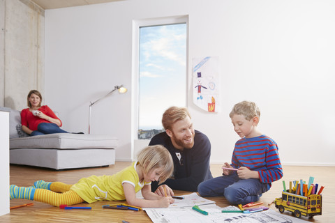 Vater auf dem Boden liegend mit malenden Kindern, lizenzfreies Stockfoto