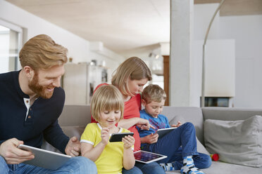 Vierköpfige Familie nutzt mobile Geräte auf der Couch - RHF001455