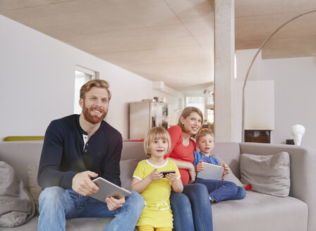 Vierköpfige Familie mit mobilen Geräten auf der Couch - RHF001456