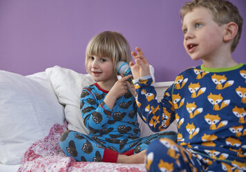 Bruder und Schwester in Pyjamas spielen mit Mikrofon - RHF001465